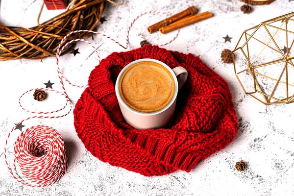 Coffee mug in a soft red winter scarf on a gray background with Christmas decorations. Christmas coffee break for home recreation. The view from the top