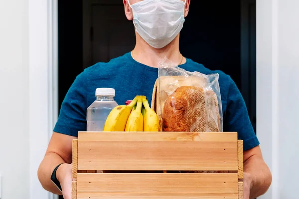 A male courier in a protective mask delivers a box of groceries. Service delivery in terms of quarantine, the concept of self-isolation