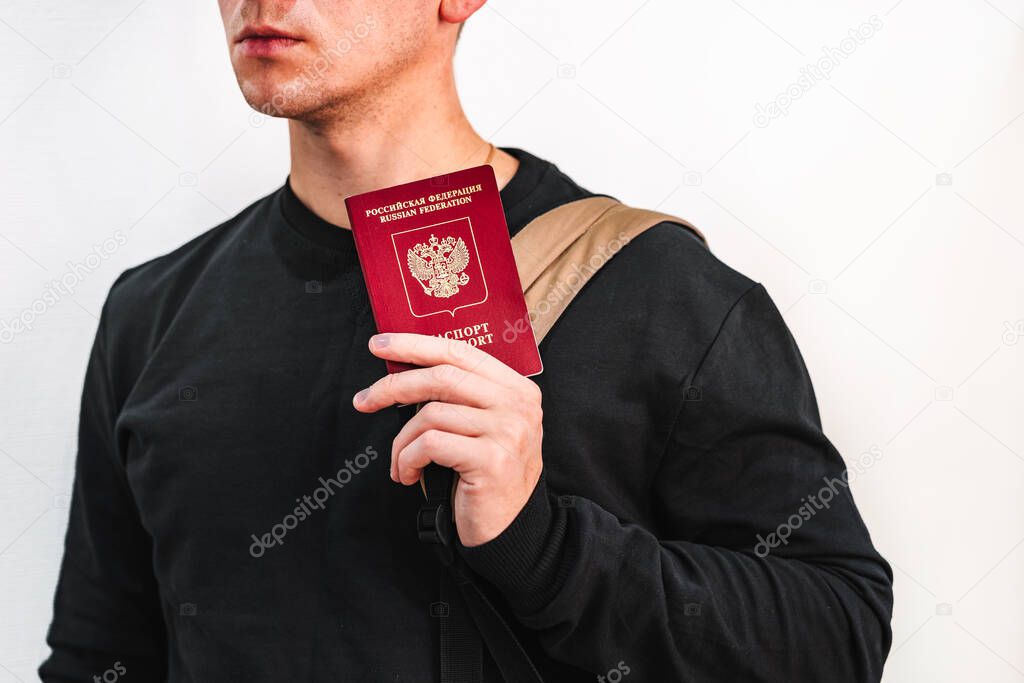 Banner on white background of a young man in a black jacket shows a Russian passport and holds a backpack .