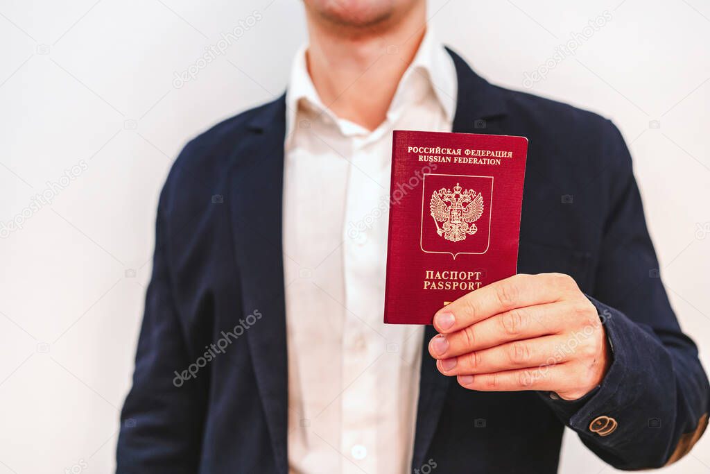 A business man in a jacket and shirt holds a Russian passport