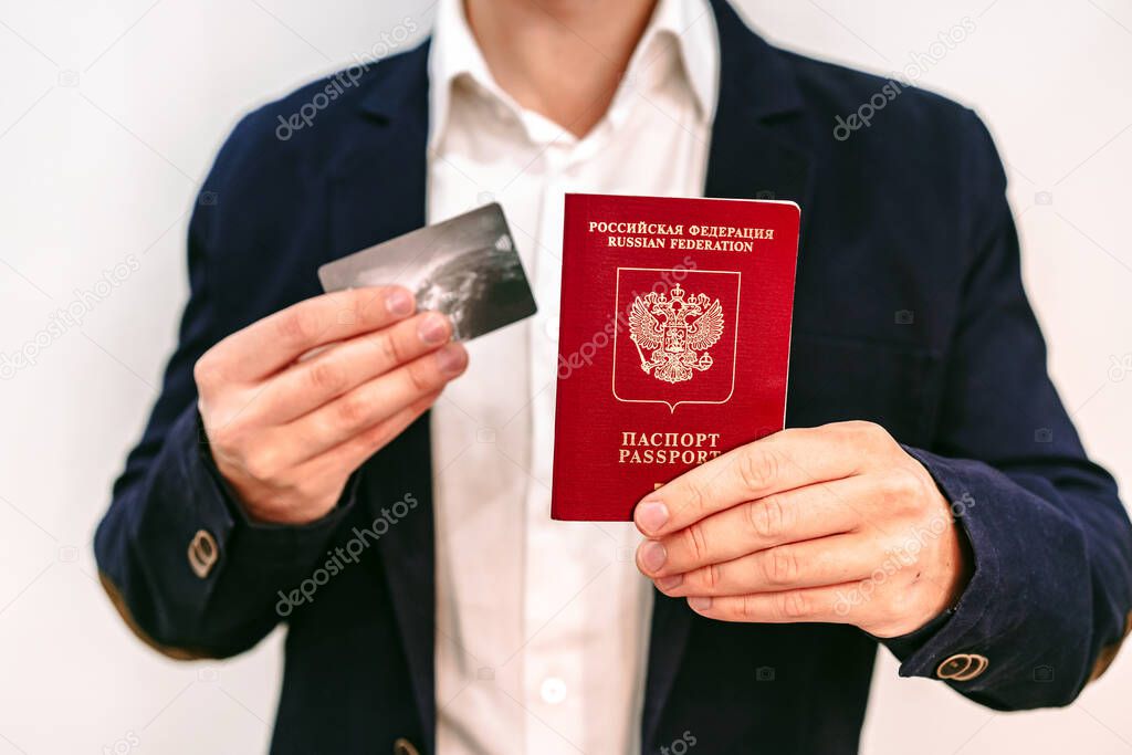 A business man in a jacket holds a Russian passport and a Bank card