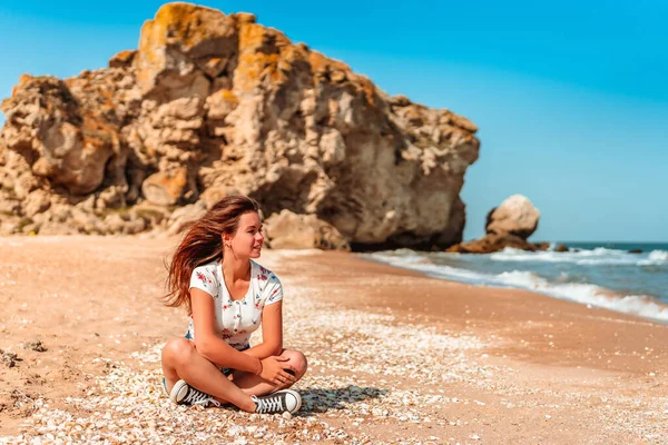 Cute young woman in skirt sitting on the sand on the beach by the sea