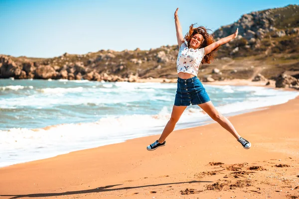 Happy young woman in a skirt jumps up and joyfully opens her hands on the beach