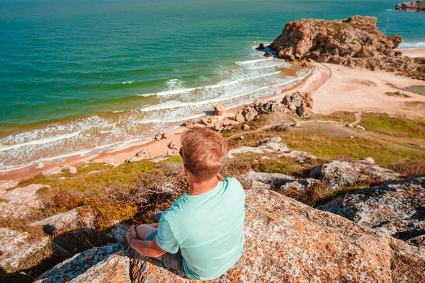 Молодой Человек Сидит Камне Спиной Камере Восхищается Бушующим Морем Посреди — стоковое фото