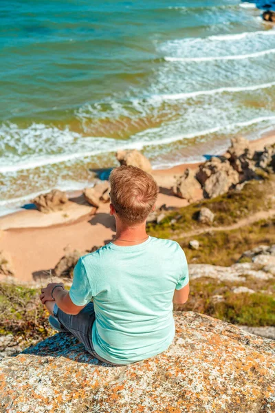 Молодой Человек Сидит Камне Спиной Камере Восхищается Бушующим Морем Посреди — стоковое фото