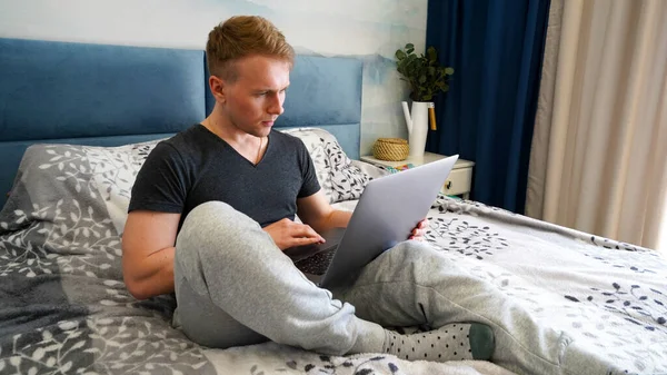 Hombre Joven Está Acostado Cama Dormitorio Azul Con Una Computadora —  Fotos de Stock
