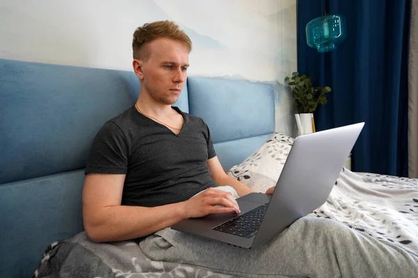 Hombre Joven Está Acostado Cama Dormitorio Azul Con Una Computadora —  Fotos de Stock