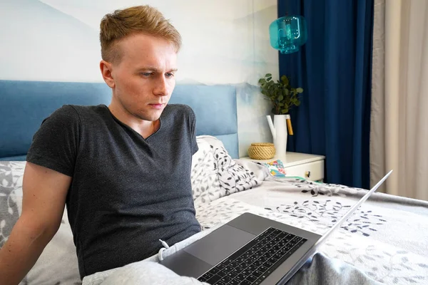 Hombre Joven Está Acostado Cama Dormitorio Azul Con Una Computadora —  Fotos de Stock