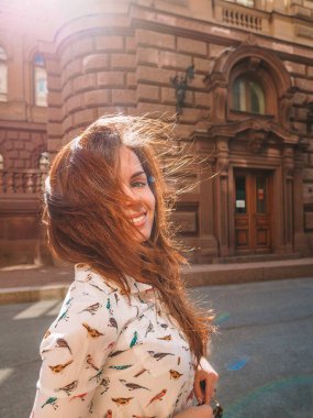 Beyaz tişörtlü, uzun saçlı bir kız St. Petersburg caddesinde güneş ışığında güzel bir tarihi binanın yanında duruyor..
