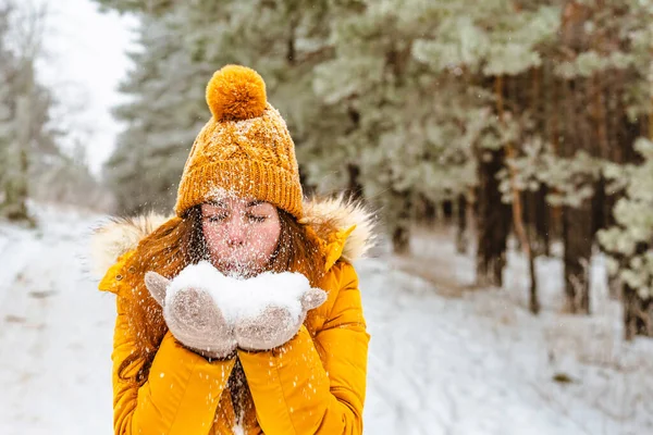 黄色のジャケットと帽子の美しい若い女性は雪の冬の森の中で雪を投げる — ストック写真