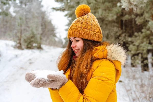黄色のジャケットと帽子の美しい若い女性は雪の冬の森の中で雪を投げる — ストック写真
