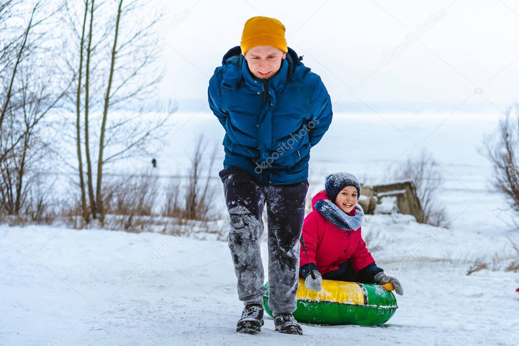 Young man drives a girl riding a tube on a snow slide, tubing winter fun