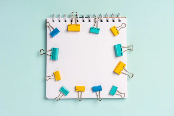 An empty blank notepad for writing on a blue background and paper clips and clips around it