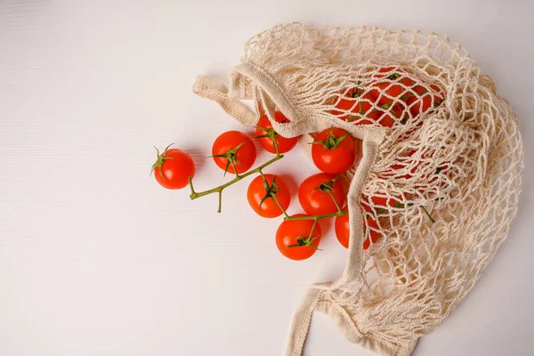 Vegetables in a beige utility mesh bag, zero waste concept. Tomatoes are red juicy ripe eco bio fresh on a white background. Farmer's Food Market. Vegan Bag