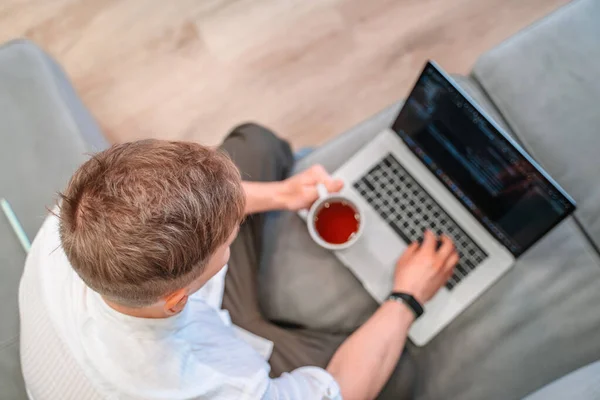 若い男性プログラマーのコーヒーを飲み ノートパソコンのキーボードに書き込みのトップビュー 家庭でテクノロジーやコンピュータを扱う人々の概念 — ストック写真