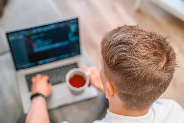 若い男性プログラマーのコーヒーを飲み ノートパソコンのキーボードに書き込みのトップビュー 家庭でテクノロジーやコンピュータを扱う人々の概念 — ストック写真