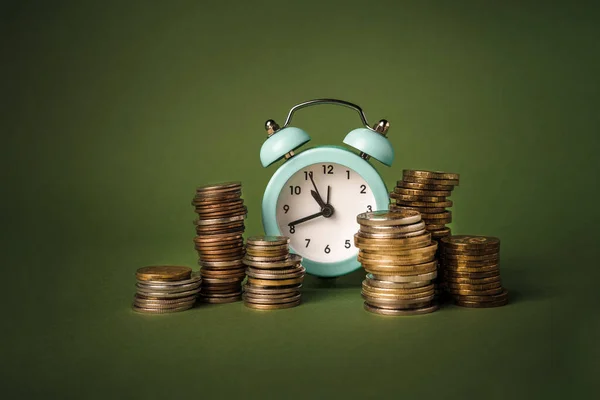 Alarm clock and stacks of coins on a green background. The concept of value time is money. A symbol of money accumulation.