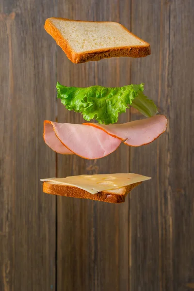 Making a sandwich. Cheese, bread and meat hang in the air in parts on a wooden background