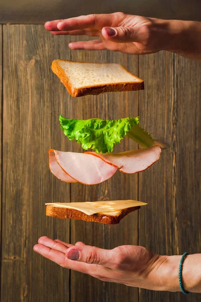 Making a sandwich. Cheese, bread and meat hang in the air in parts on a wooden background