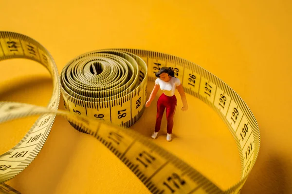 Miniature people on a yellow background, a woman in a maze of measuring tape, the concept of diet and weight loss