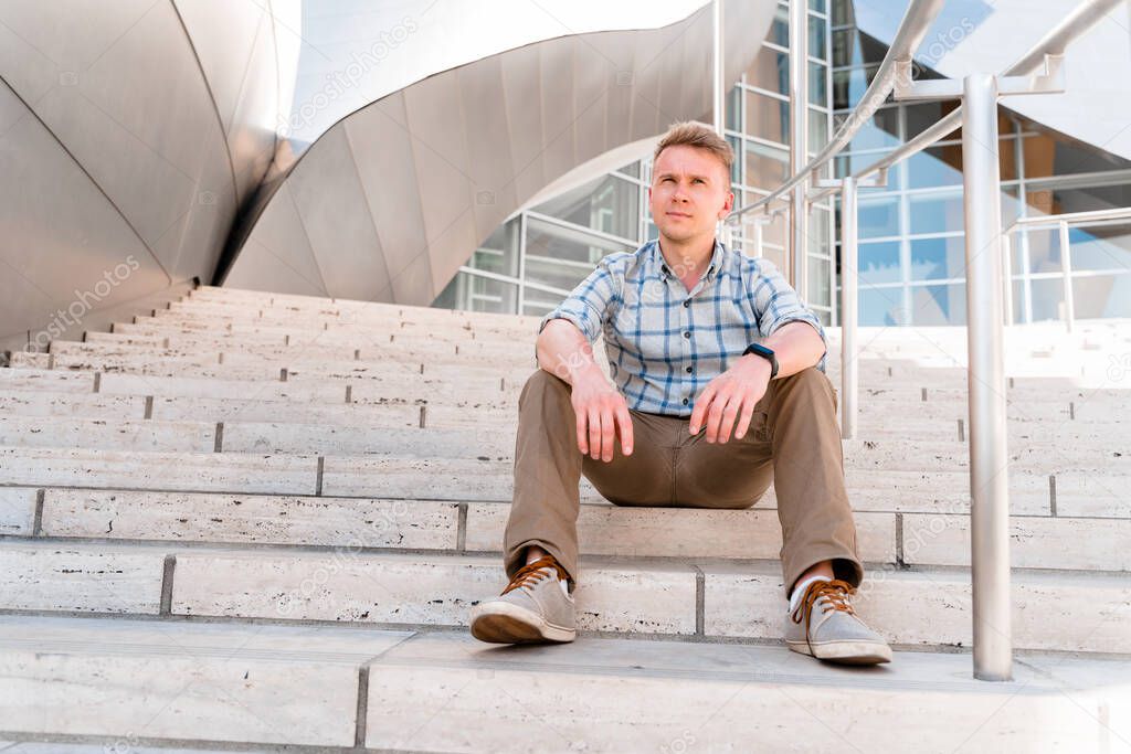 A young blond man in sunglasses stands on the steps of the Walt Disney Concert Hall. Business style in a trendy building, Los Angeles
