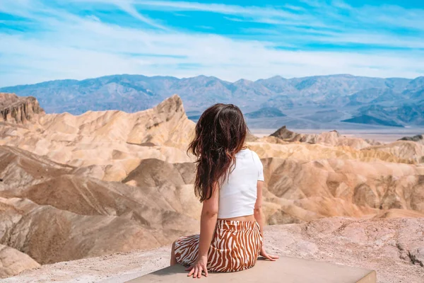 A beautiful young woman in a skirt stands in the middle of a desert landscape in Death Valley Zabriskie Point, USA.