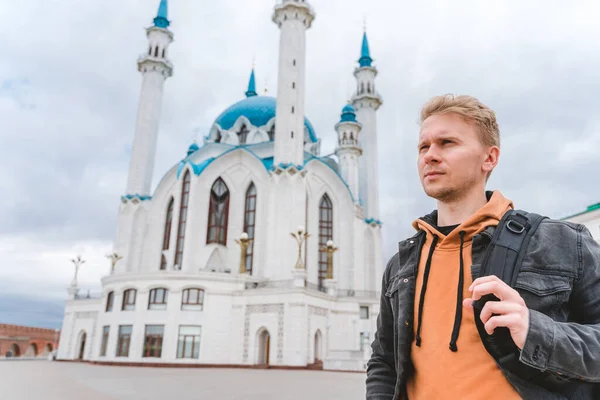 A young male blonde tourist stands in front of a mosque on a cloudy day, Kazan, Russia