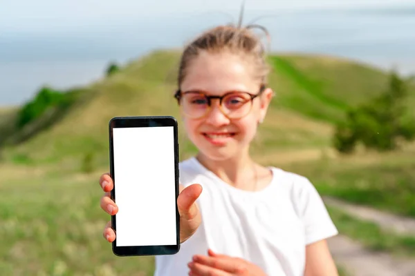 笑顔の女の子は夏の公園で空白の携帯電話の画面を示しています 空白の画面上のテキストのスペース — ストック写真