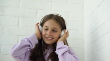 4k video. Küçük tatlı bir kız çocuğu kulaklıkla müzik dinliyor ve dans ediyor.
