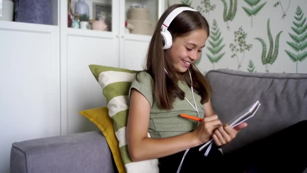 Nagranie Mała Dziewczynka Siedzi Kanapie Używa Słuchawek Studiując Wykłady Pisząc — Wideo stockowe