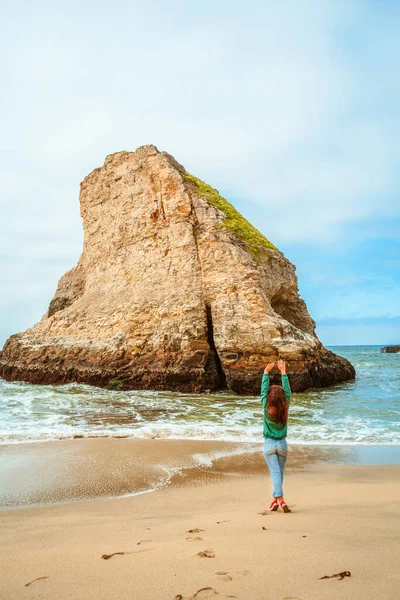 A young woman in a green jacket walks along the picturesque beach of Shark Fin Bay on the California coast