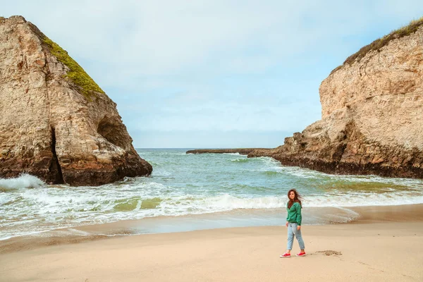 A young woman in a green jacket walks along the picturesque beach of Shark Fin Bay on the California coast