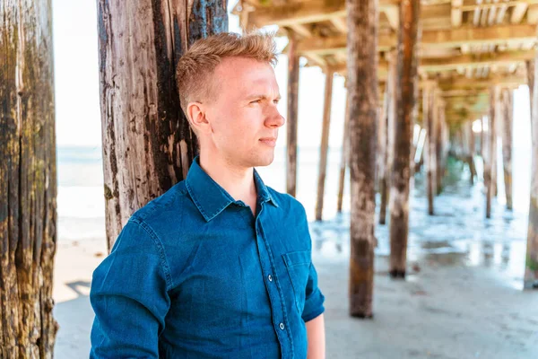 A handsome young man poses under a pier in Capitola, California