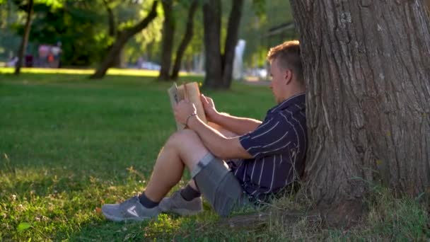Nagranie Młody Człowiek Siedzi Pod Drzewem Trawie Parku Czyta Książkę — Wideo stockowe