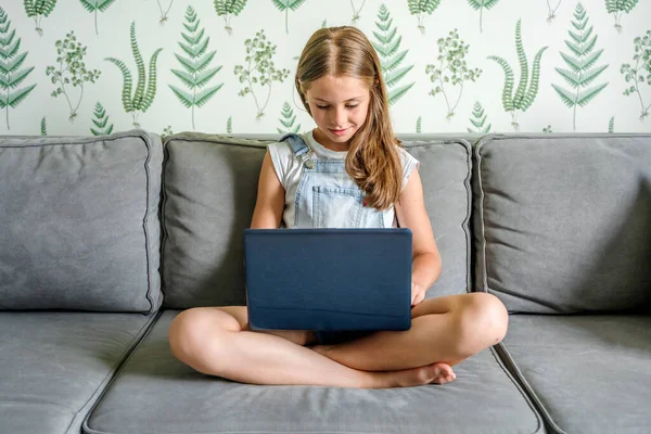 小さな女の子がリビングルームのソファに座って ラップトップを使って自宅で勉強しています デジタル教育 コンピュータ技術 ソーシャルメディア インターネット — ストック写真