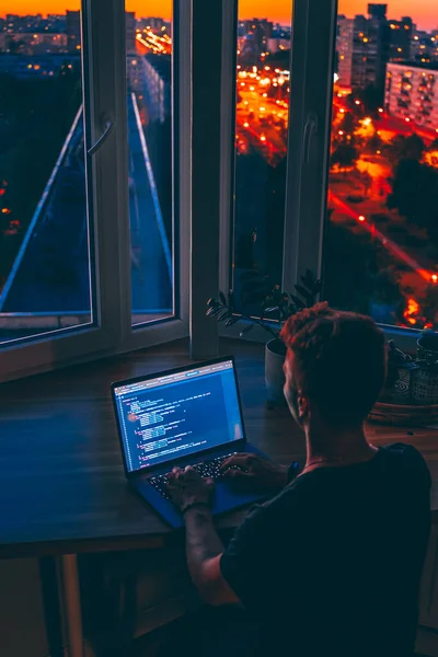 若い男性開発者は夜遅くにコードスクリプトをプログラミングしています美しい都市のライトと夜 — ストック写真