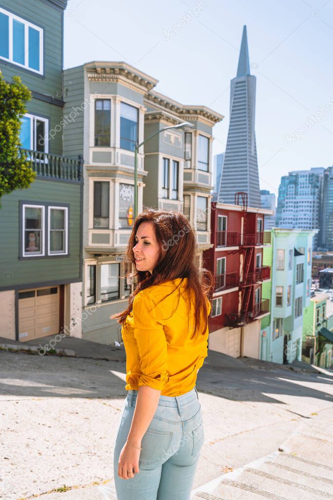 Cute young woman walks along a beautiful street with a view of the Transamerica Tower in San Francisco