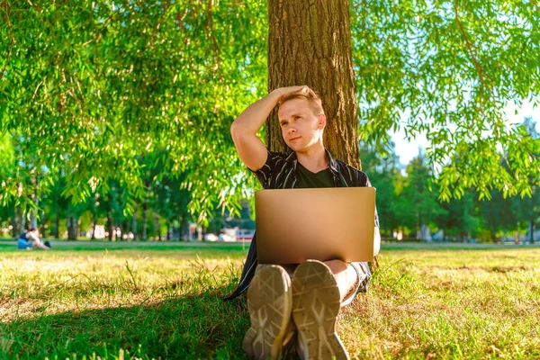 Een Jongeman Zit Onder Een Boom Werkt Met Een Laptop — Stockfoto