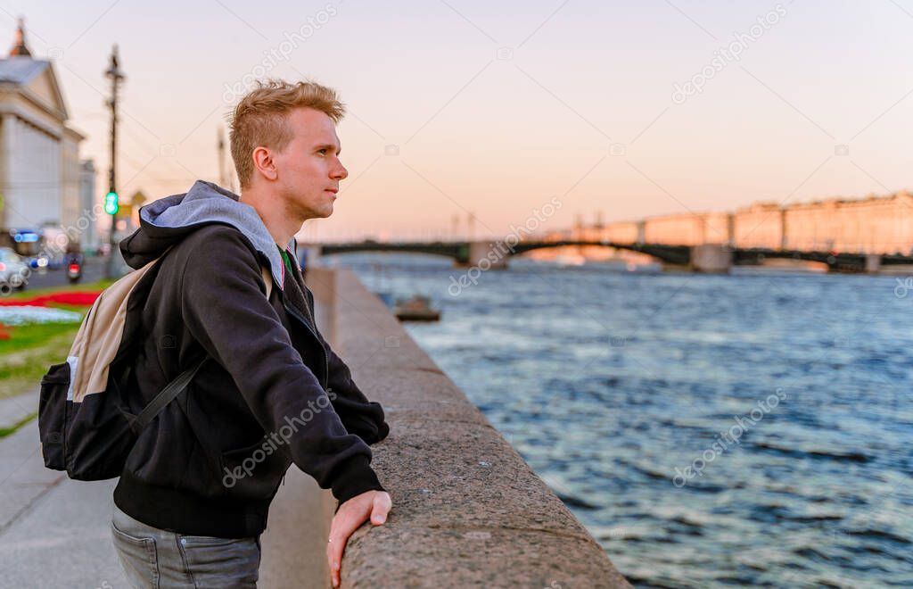 A young man stands on the embankment in St. Petersburg at sunset with a view of St. Isaac's Cathedral