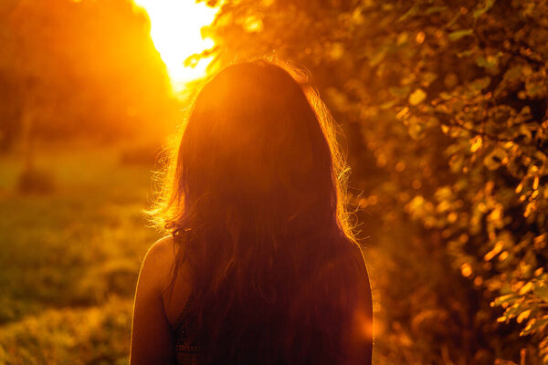 A young woman walks along a path in the park at sunset. Amazing natural landscape