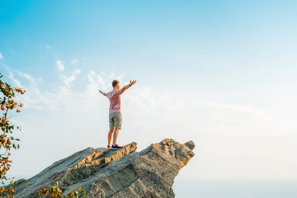 A young athletic man stands on a picturesque steep cliff above the sea against the sky in Crimea. The concept of travel and freedom.