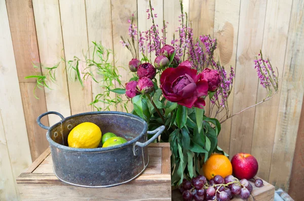 Stillleben roter Pfingstrosen mit Früchten auf hölzernem Hintergrund — Stockfoto