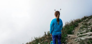 Arkadan gelen kızın kafasında mavi bir ceketle dağlardaki sisin içinde boynuzlar vardı. Eğlence konsepti, dağlarda yürüyüş, yürüyüş, aktif yaşam tarzı.