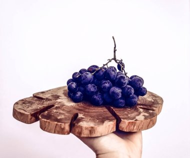 Koyu mavi üzümlerden oluşan bir demet, beyaz arka planda, ahşap bir tahtanın üzerinde su damlaları halinde.