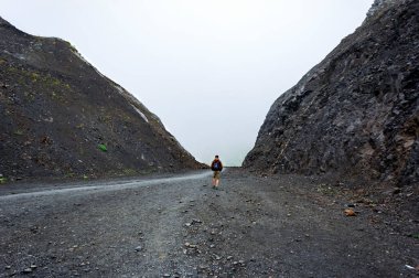 Sırt çantalı genç adam iki kayanın arasındaki yolda yürüyor. Dağ yürüyüşü, yalnız seyahat, yürüyüş, aktif yaşam tarzı,