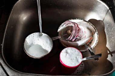 Sabunlu köpüklü bulaşıklar metal mutfak lavabosunda ve musluktan gelen su akıntısı, ev işi, seçici odaklanma