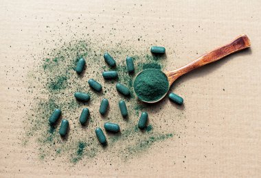 Organik klorella, spirulina ya da tahta kaşıkta arpa tozu ve bej kağıda yazılmış haplar. Besin takviyesi, detoks süper gıdalar, sağlıklı yaşam tarzı.