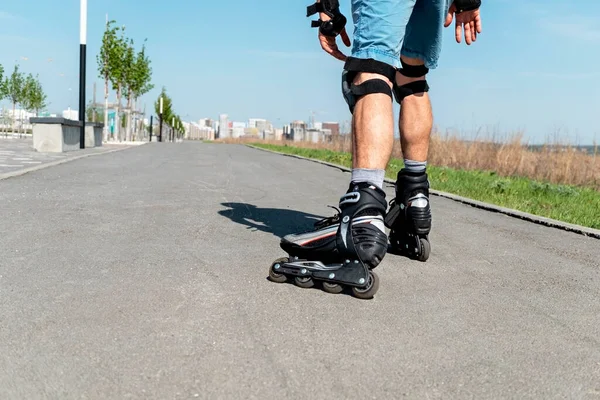 夏季，穿着旱冰鞋和防护用品的男子腿在沥青路面上近距离滑行 免版税图库图片