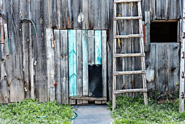 Köy mavisi ahşap duvarda köpek geçidi kapısı ve ahşap merdiven girişi üzerinde beyaz at nalı, yıpranmış ev.