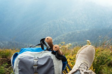 Sırt çantası, yürüyüş direkleri ve spor ayakkabıları vadide bir dağ yürüyüşünde dinlenen genç bir kadın, açık havada aktif sağlıklı bir yaşam tarzı.